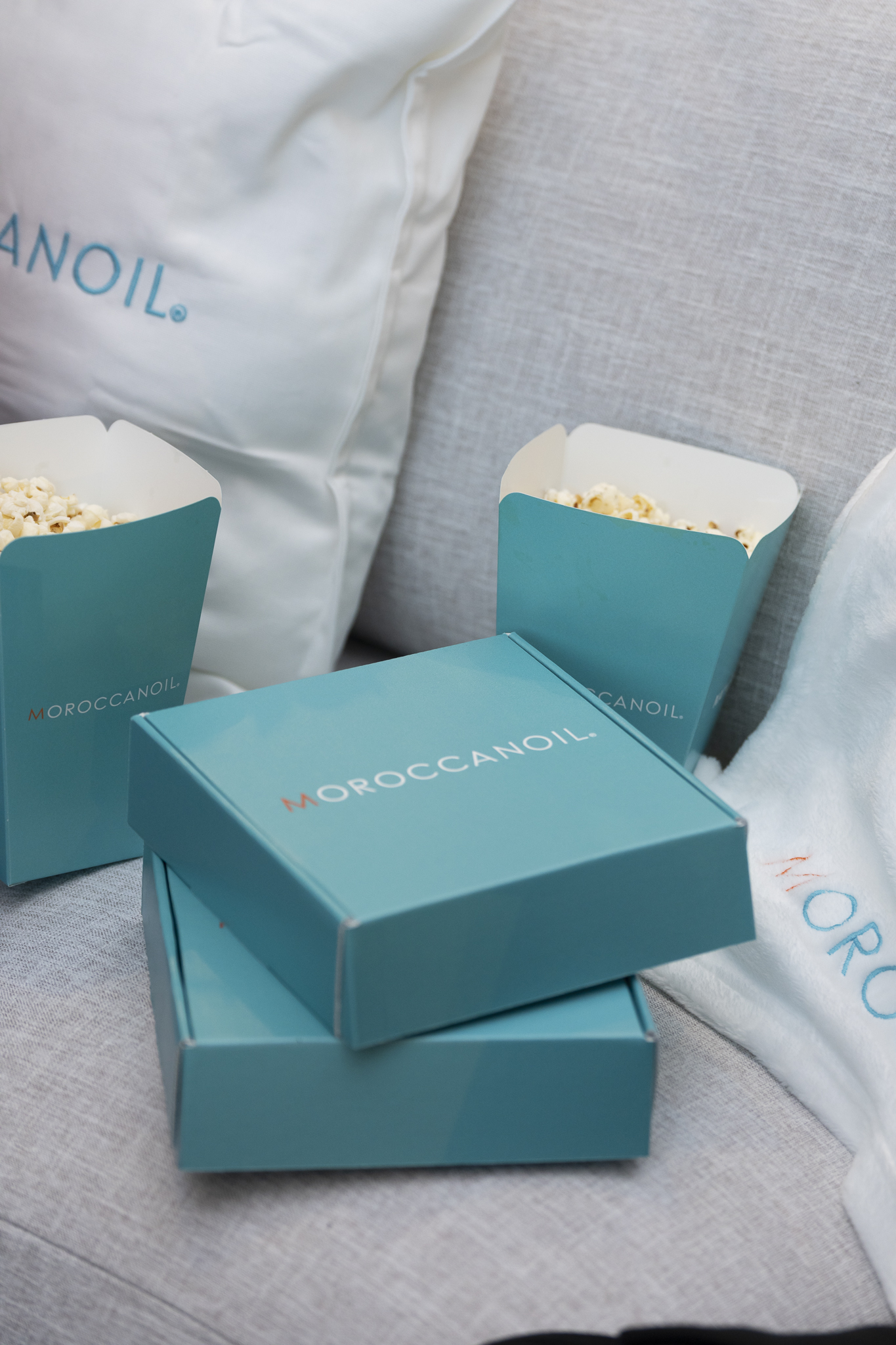 Open teal Moroccanoil gift boxes with popcorn cups on a gray fabric surface with a white pillow nearby.
