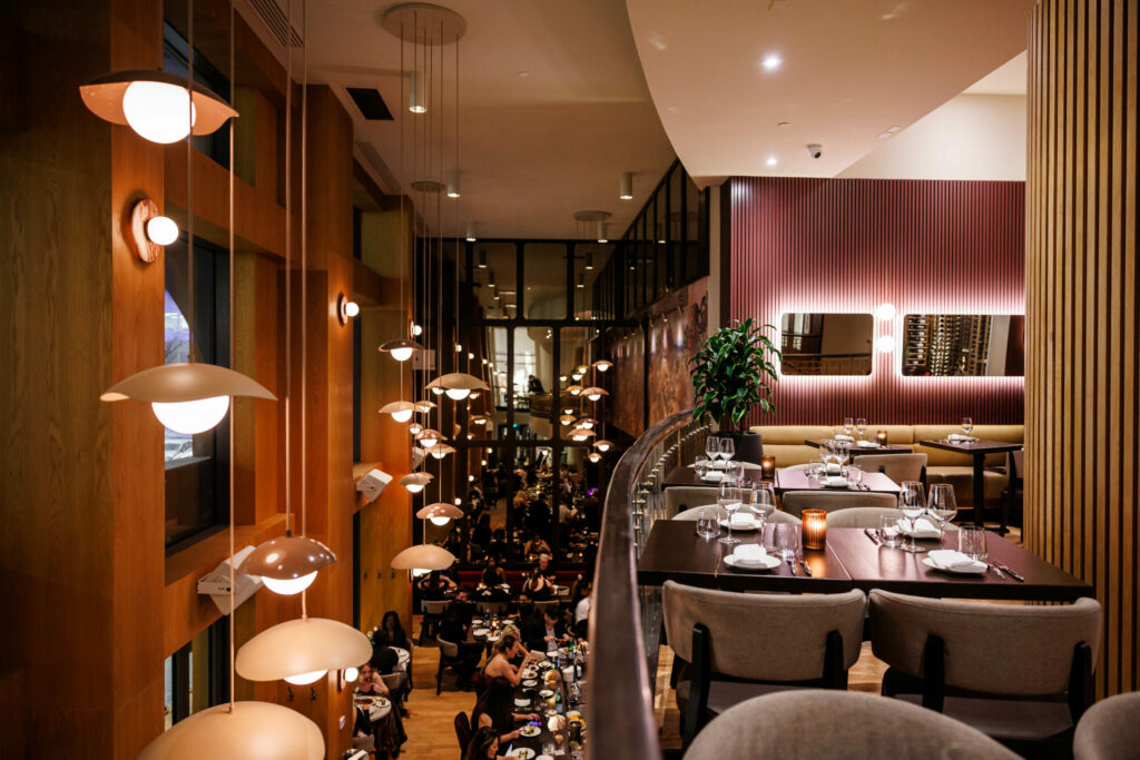 Restaurant dining area with warm pendant lights, wooden walls, and tables set for guests.