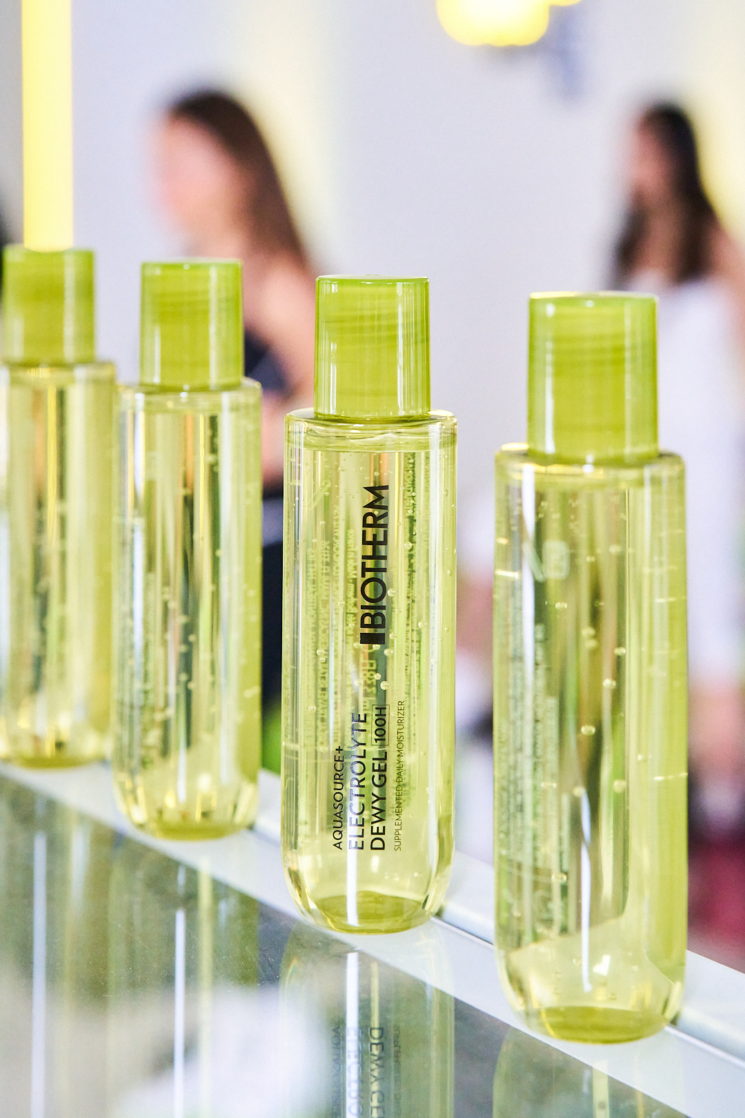 Row of lime-green-capped cosmetic bottles on a glass display, central bottle labeled Biotherm.