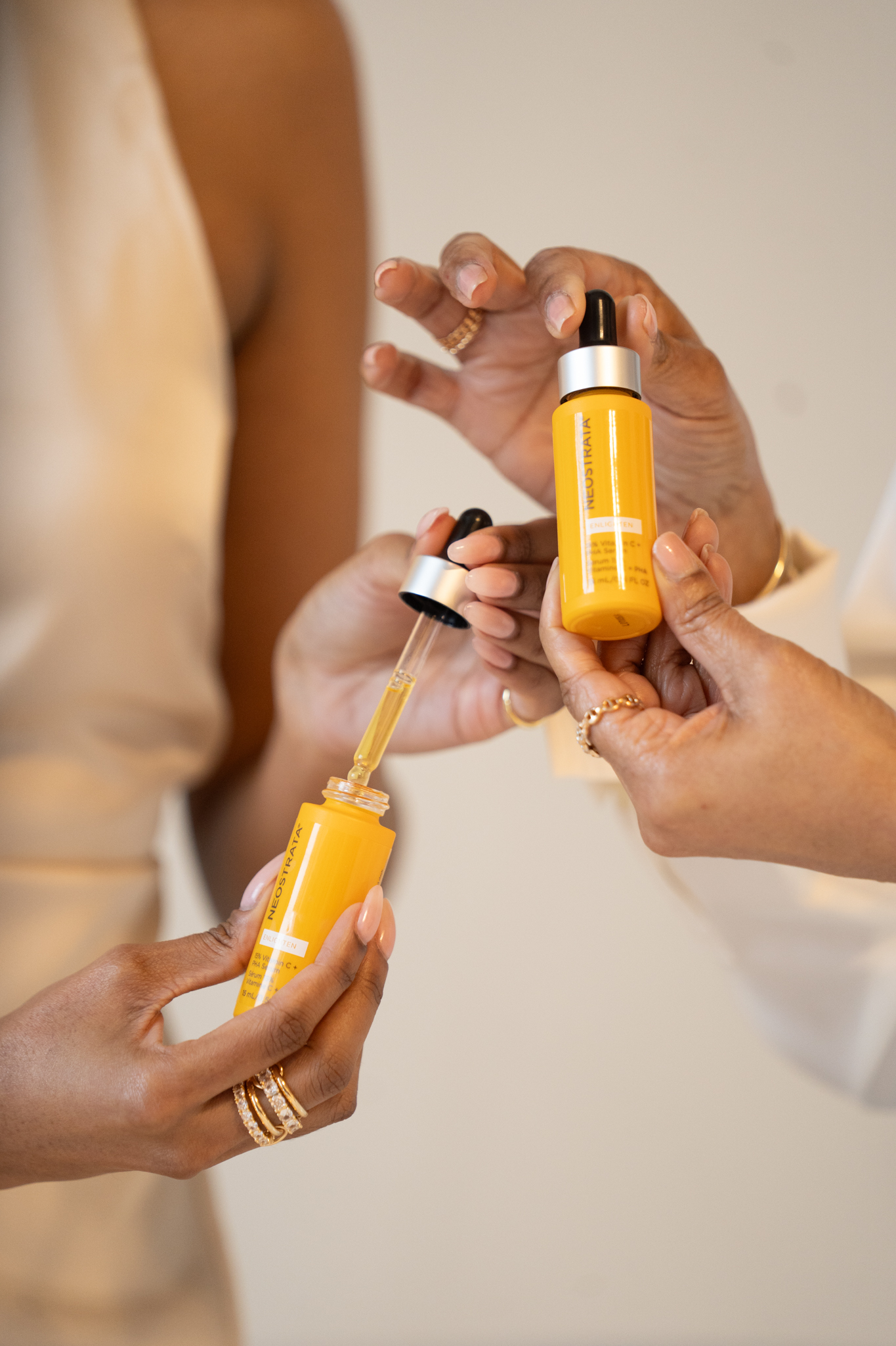 Two people share a skincare routine: orange-yellow serum bottles and droppers are being used.